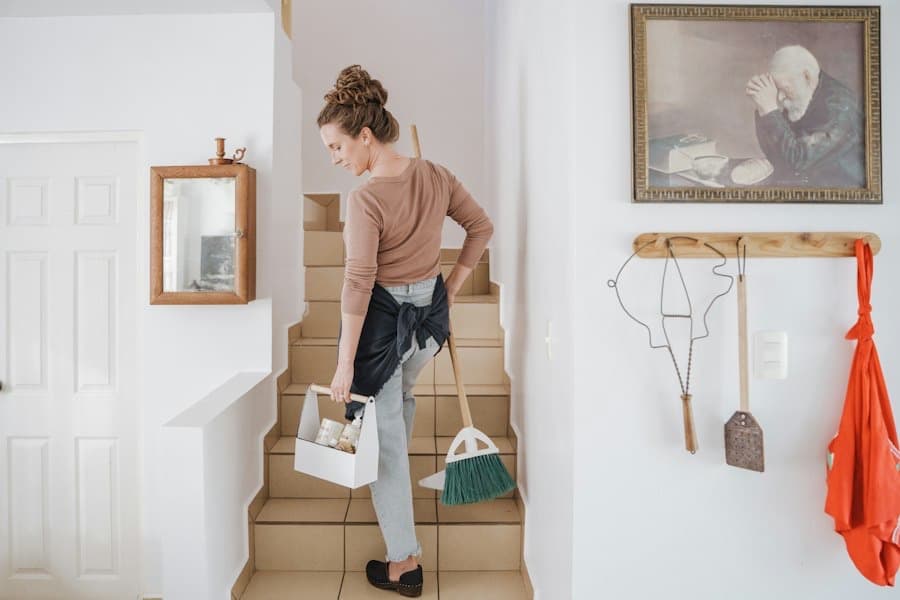 A cleaner carrying her caddy and broom up a flight of stairs