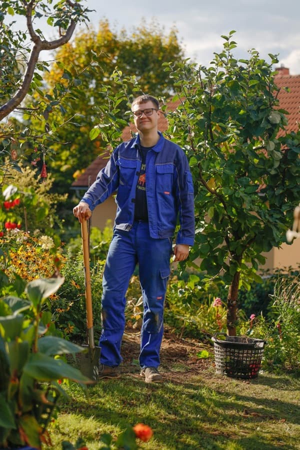 A gardener in work clothes leaning on his spade in a garden