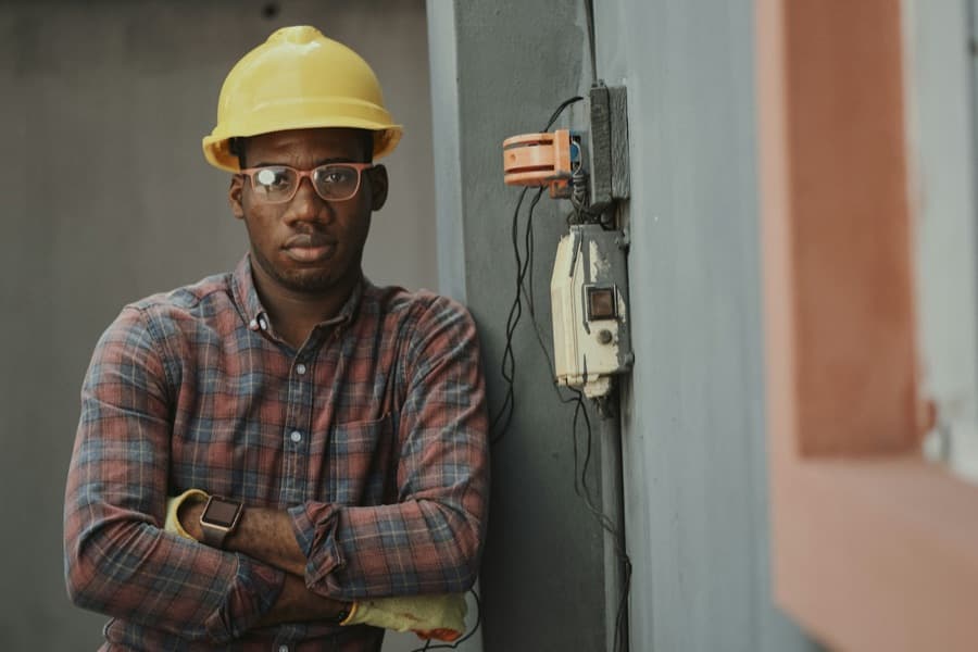 An electrician in a hard hat beside a fuse box