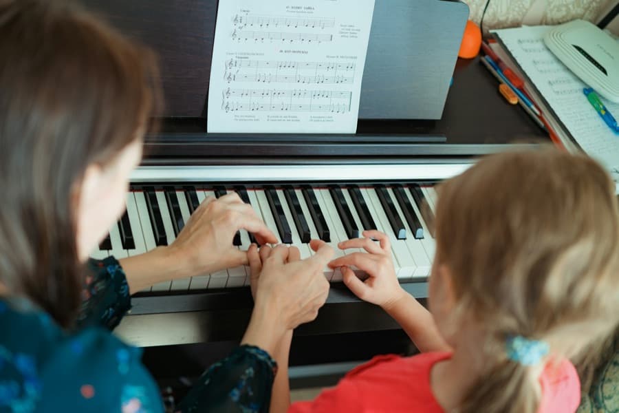 A piano teacher guiding a child's hands on the keys
